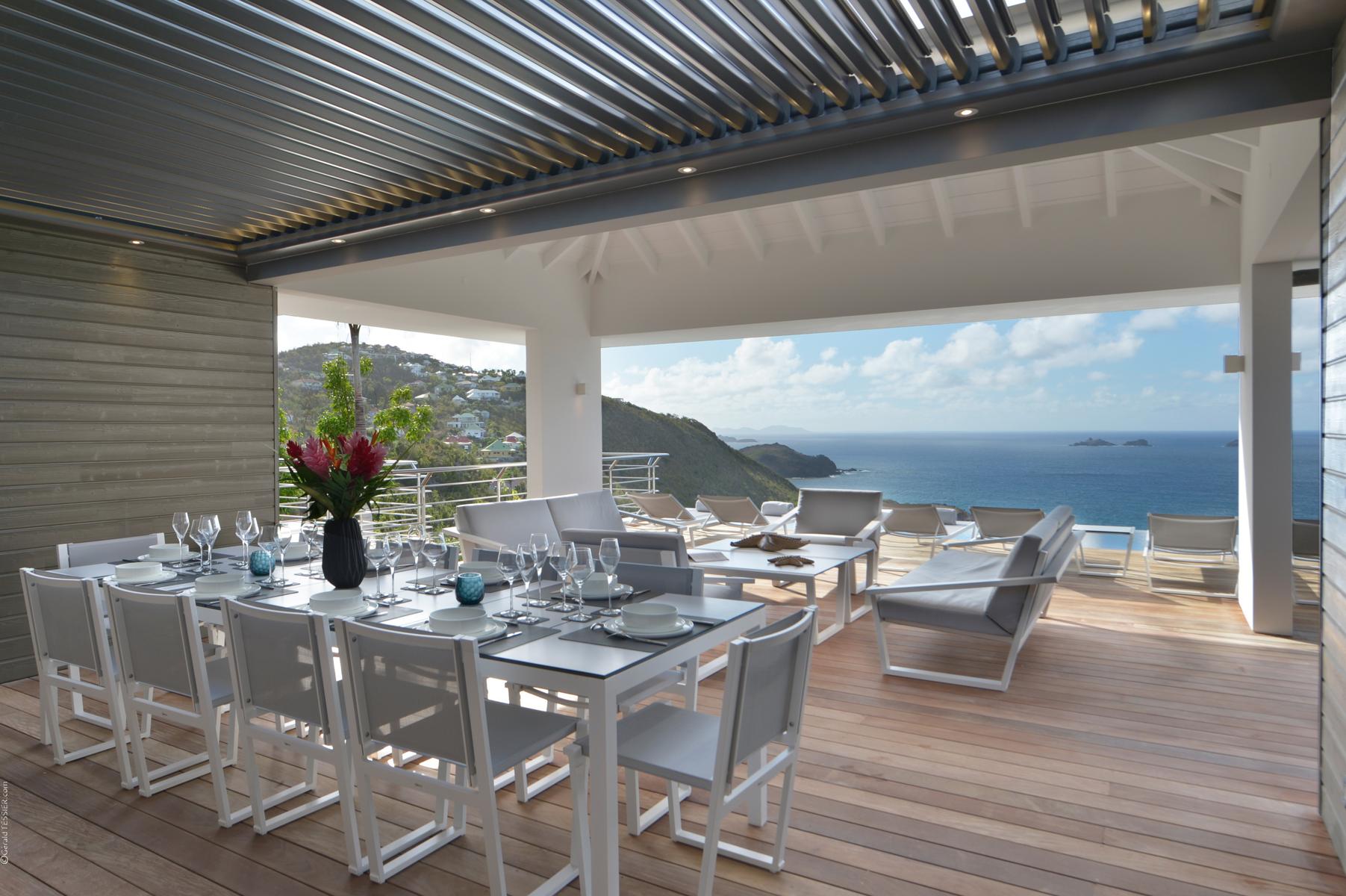 Covered outdoor dining terrace in a St Barts villa with elegant table setting, lounge chairs, and sweeping ocean views.