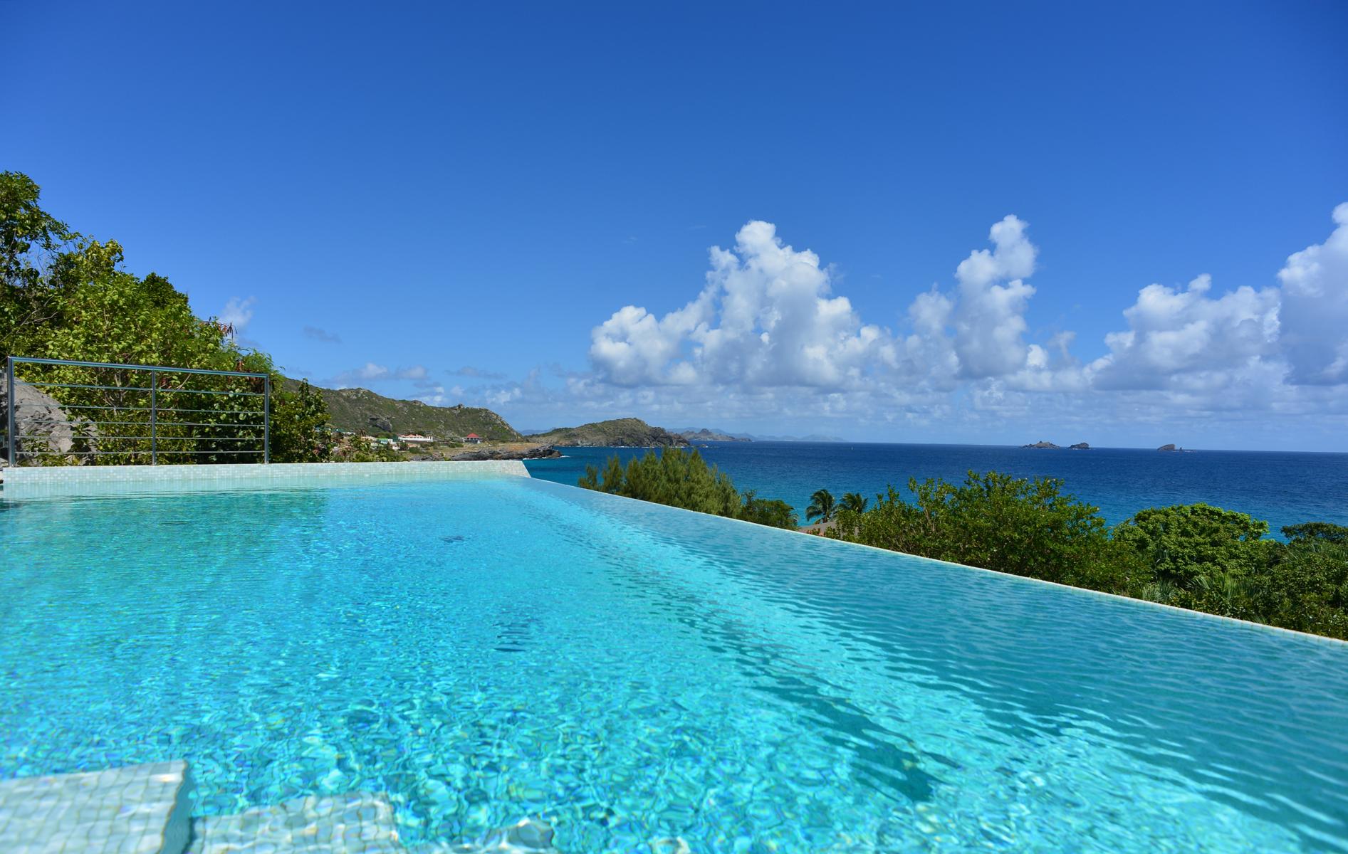Infinity pool with panoramic ocean view and tropical hillside backdrop at luxury villa in St Barts