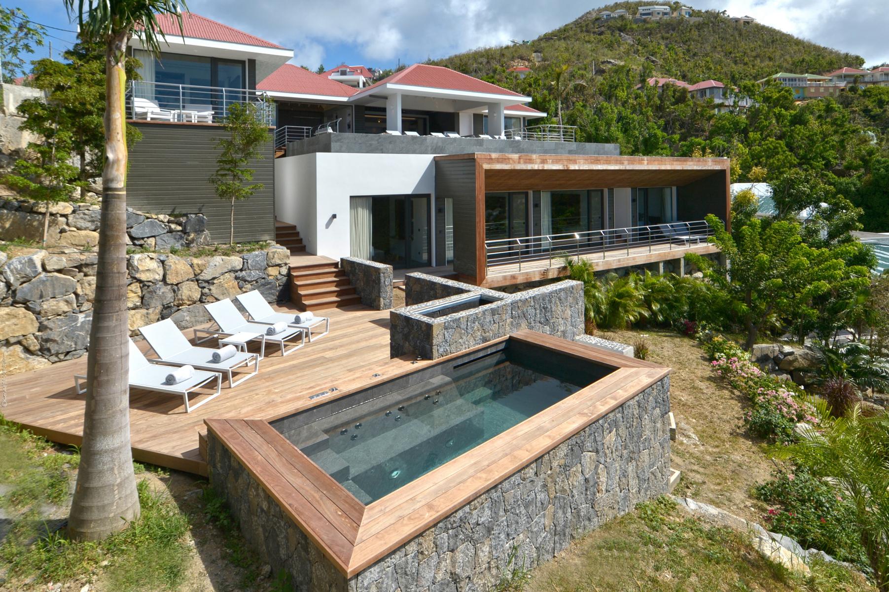 Stone terrace of a St Barts villa with plunge pool, sun loungers, and hillside views surrounded by tropical greenery.