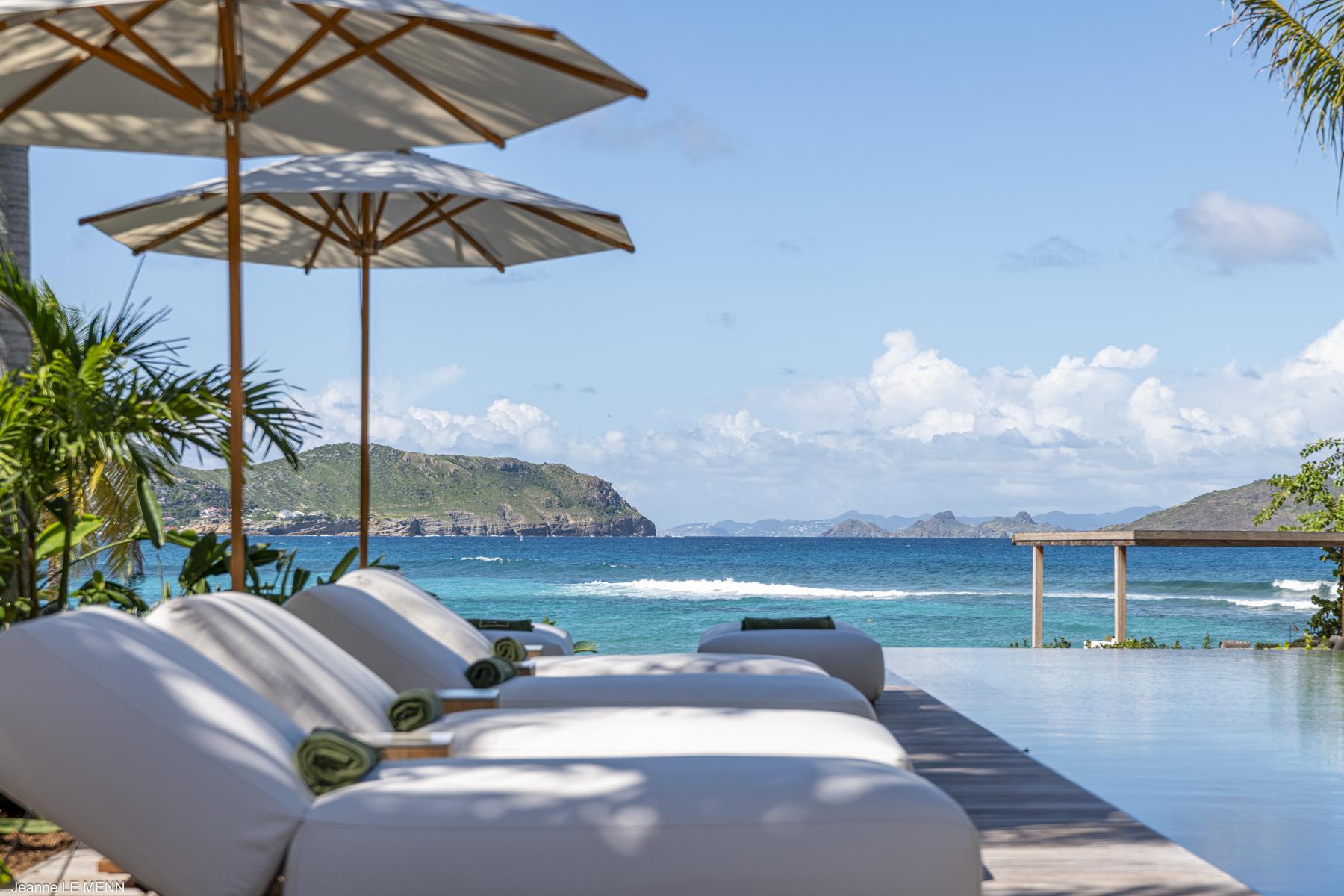 Poolside loungers with umbrellas at a St Barts villa overlooking turquoise waters and distant islands.