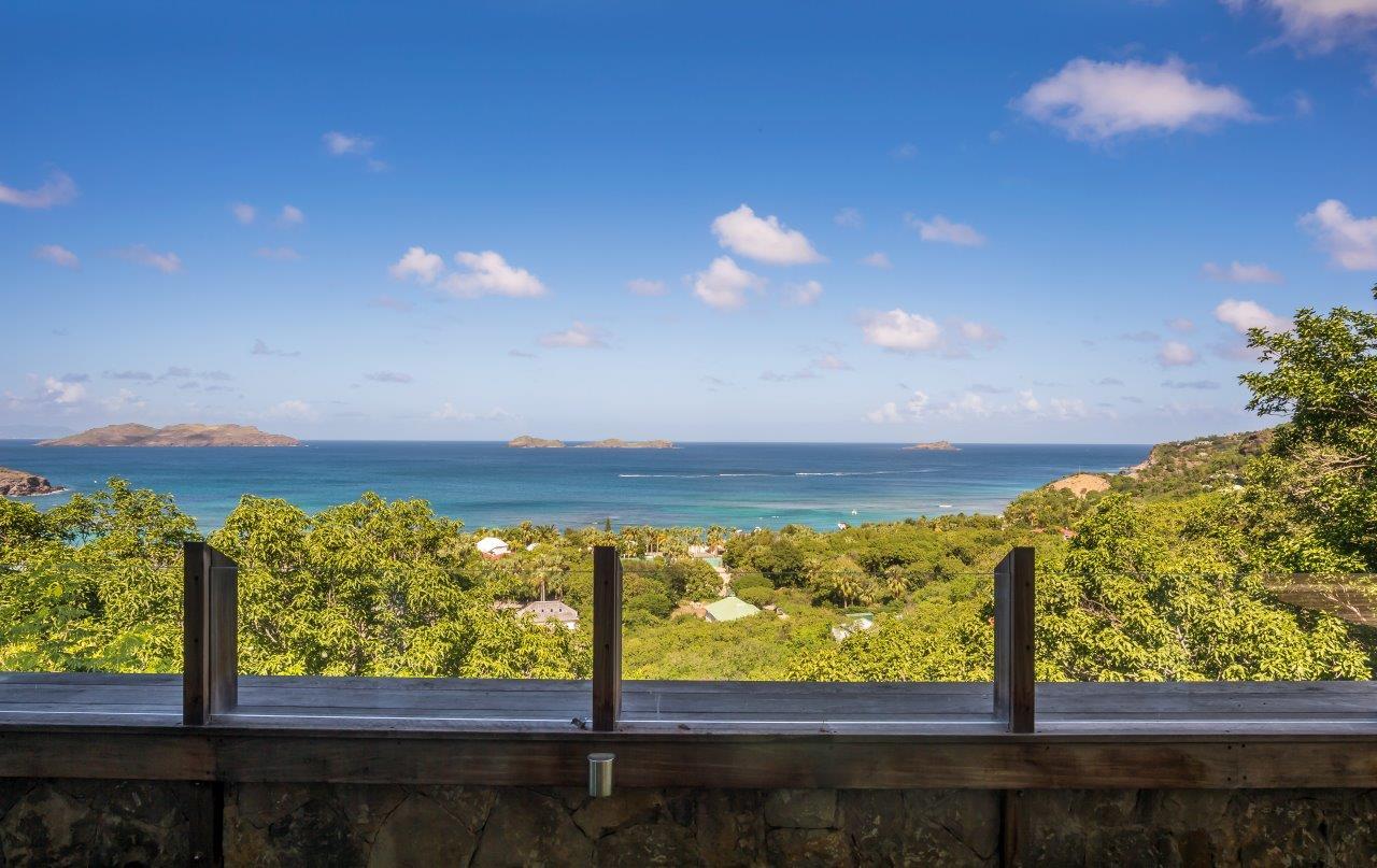 Expansive ocean view from a St Barts villa terrace, with lush green hills leading to turquoise waters and distant islands under a clear sky.