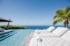 Luxury infinity pool at a St Barts villa with cushioned white loungers, palm tree, and panoramic ocean views.