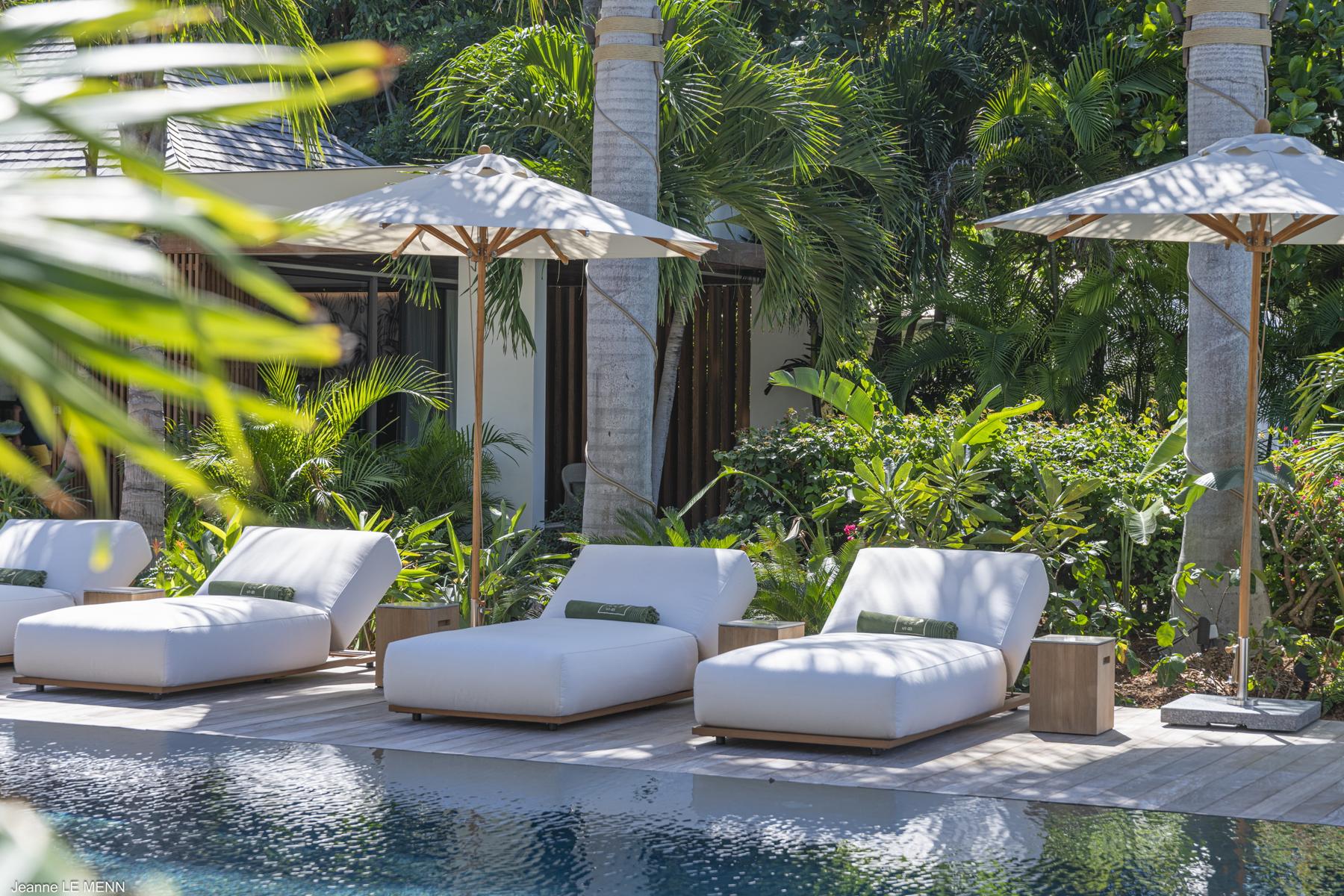 Poolside loungers with umbrellas at a tropical St Barts villa surrounded by lush greenery.