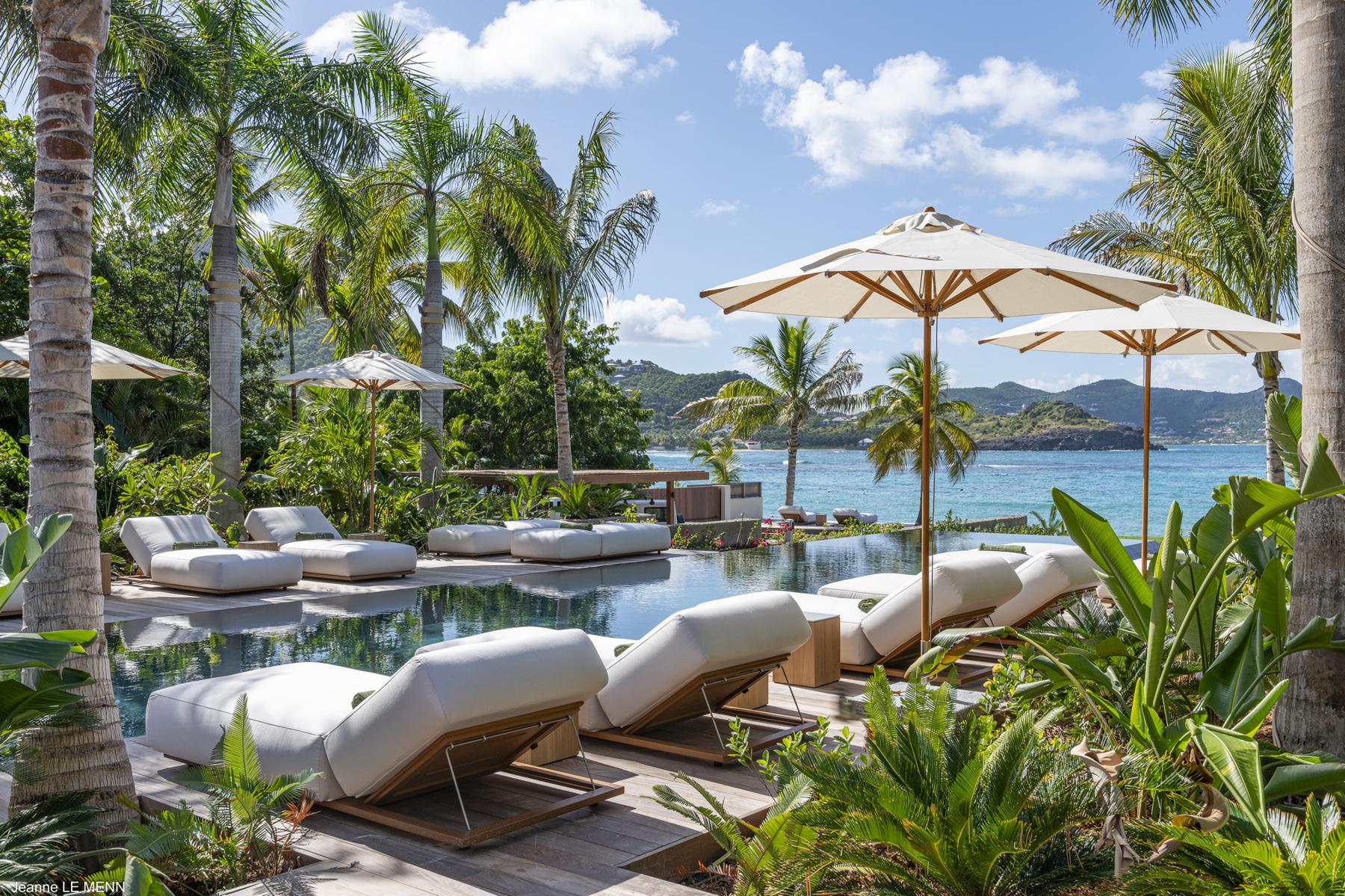 Luxury poolside loungers with umbrellas at a St Barts villa surrounded by palm trees and overlooking the sea