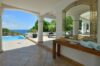 Shaded terrace of a St Barts villa with arched columns, ocean-view pool, and elegant wooden console table with mirror.