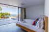 Modern bedroom in a St Barts villa with floor-to-ceiling glass doors opening to a pool terrace and ocean panorama.