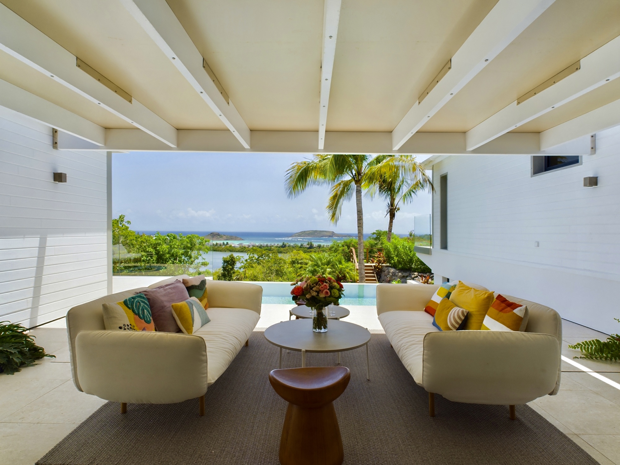 Stylish covered lounge at a St Barts vacation rental with ocean view framed by palm trees.