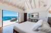 Sunlit bedroom in a St Barts villa with oceanfront terrace, white linens, and panoramic sea views through sliding doors.