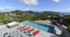 Hillside pool terrace at a St Barts villa with red sun loungers, jacuzzi, and panoramic views of lush valleys and the sea.