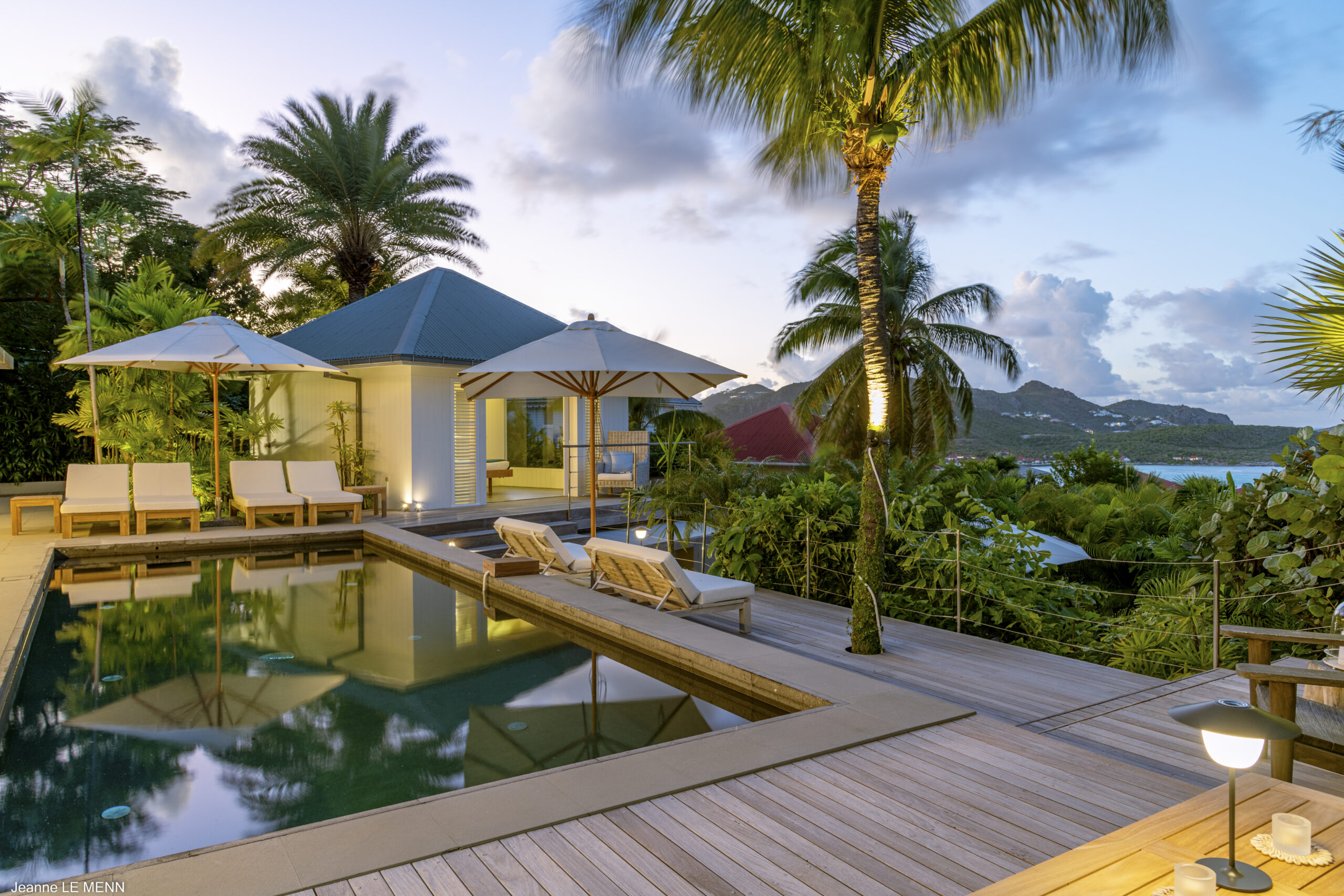 Luxury villa pool deck with sun loungers, palm trees, and ocean views at sunset in St Barts vacation rental.