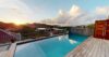 Infinity pool with wooden deck overlooking sunset skies and hillsides at a tranquil St Barts villa rental.