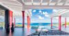 Covered terrace at a St Barts villa with bold red columns, lounge seating, and panoramic ocean views under a bright blue sky.