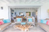 Airy open-plan lounge in a St Barts villa with wicker sofas, colourful cushions, and glass coffee table with driftwood base.
