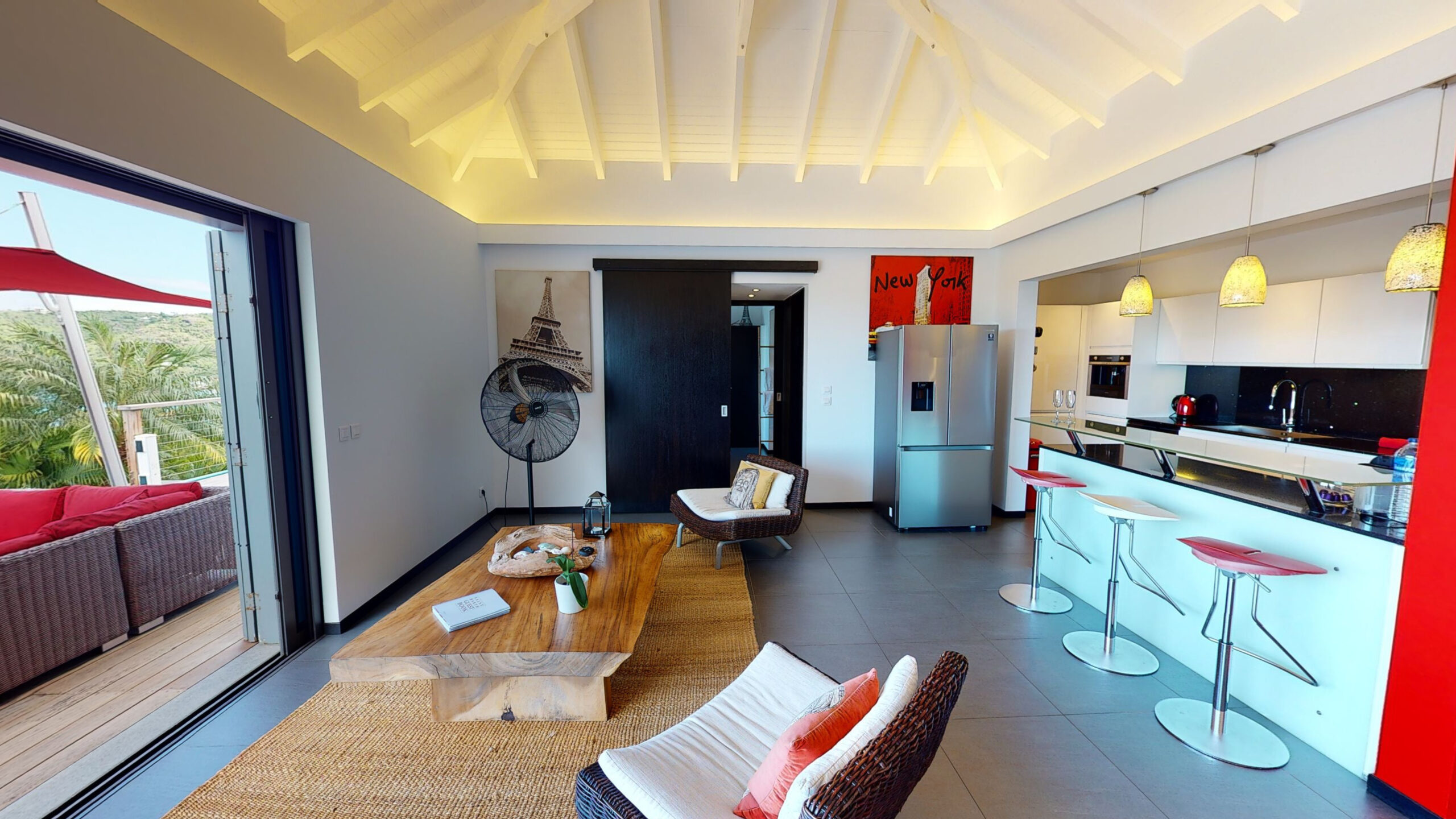 Modern open-plan villa living room with sleek kitchen, red bar stools, and access to a sunlit terrace in St Barts.
