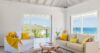 Bright living room with neutral sofas, yellow accents, and panoramic ocean views in a modern St Barts villa rental
