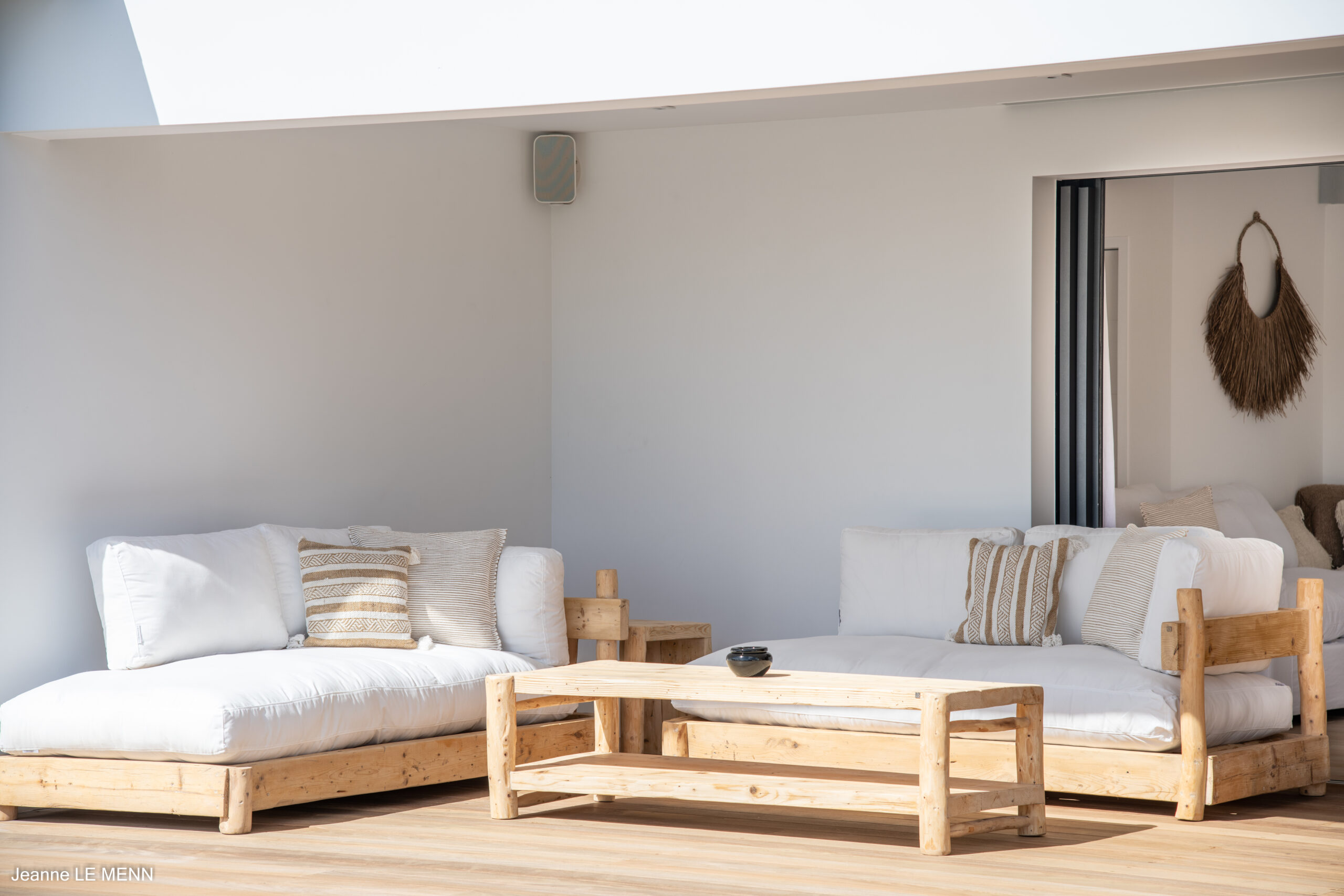 Minimalist villa lounge with natural wood sofas, white cushions, and soft neutral accents creating a calm, sunlit retreat.