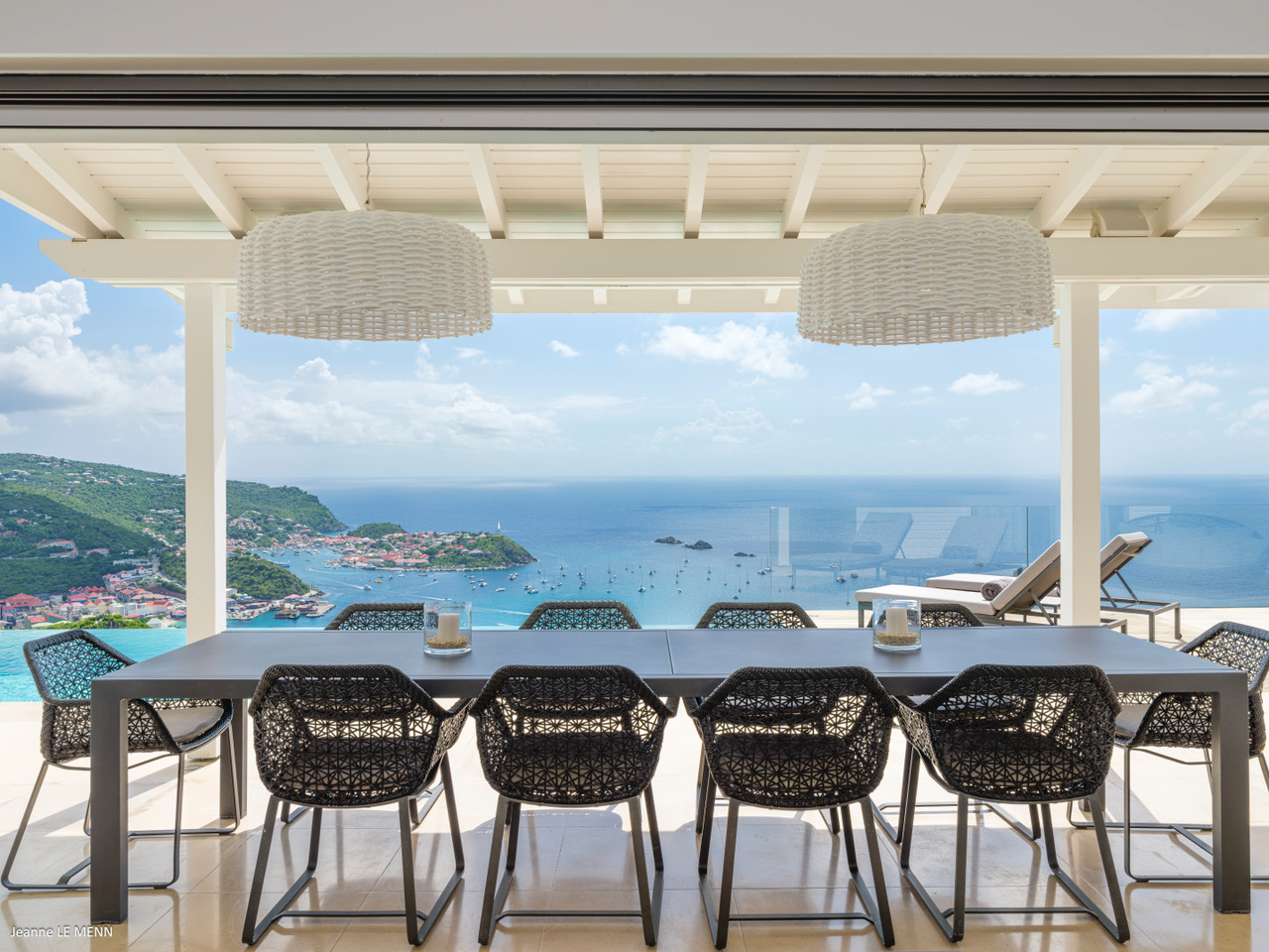Outdoor dining terrace in a St Barts villa with woven chairs, long table, and sweeping views over the Caribbean Sea.
