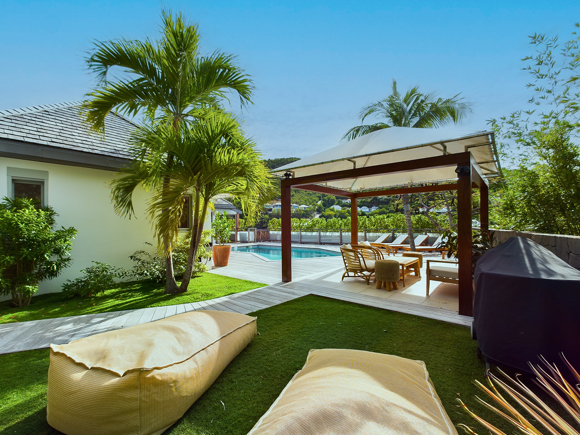 Relaxed garden lounge at a St Barts vacation rental with shaded poolside cabana and palm trees.