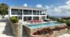 Modern St Barts villa with hillside pool terrace, red sun loungers, and stone walls adorned with vibrant tropical flowers.