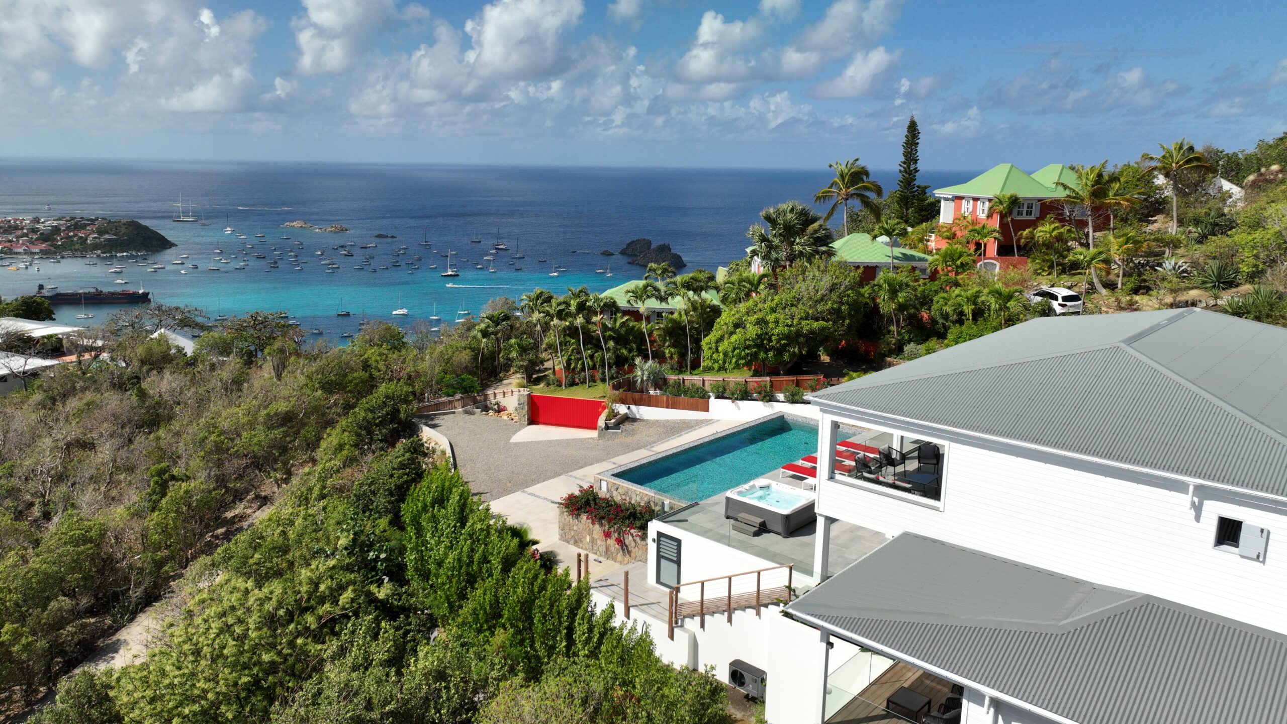 A high-angle aerial photo of a modern villa nestled in the green hills, with a panoramic view of the port of Gustavia and the harbor below.