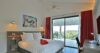 Cozy bedroom in a St Barts villa with red curtains, private terrace access, and hillside views through sliding glass doors.