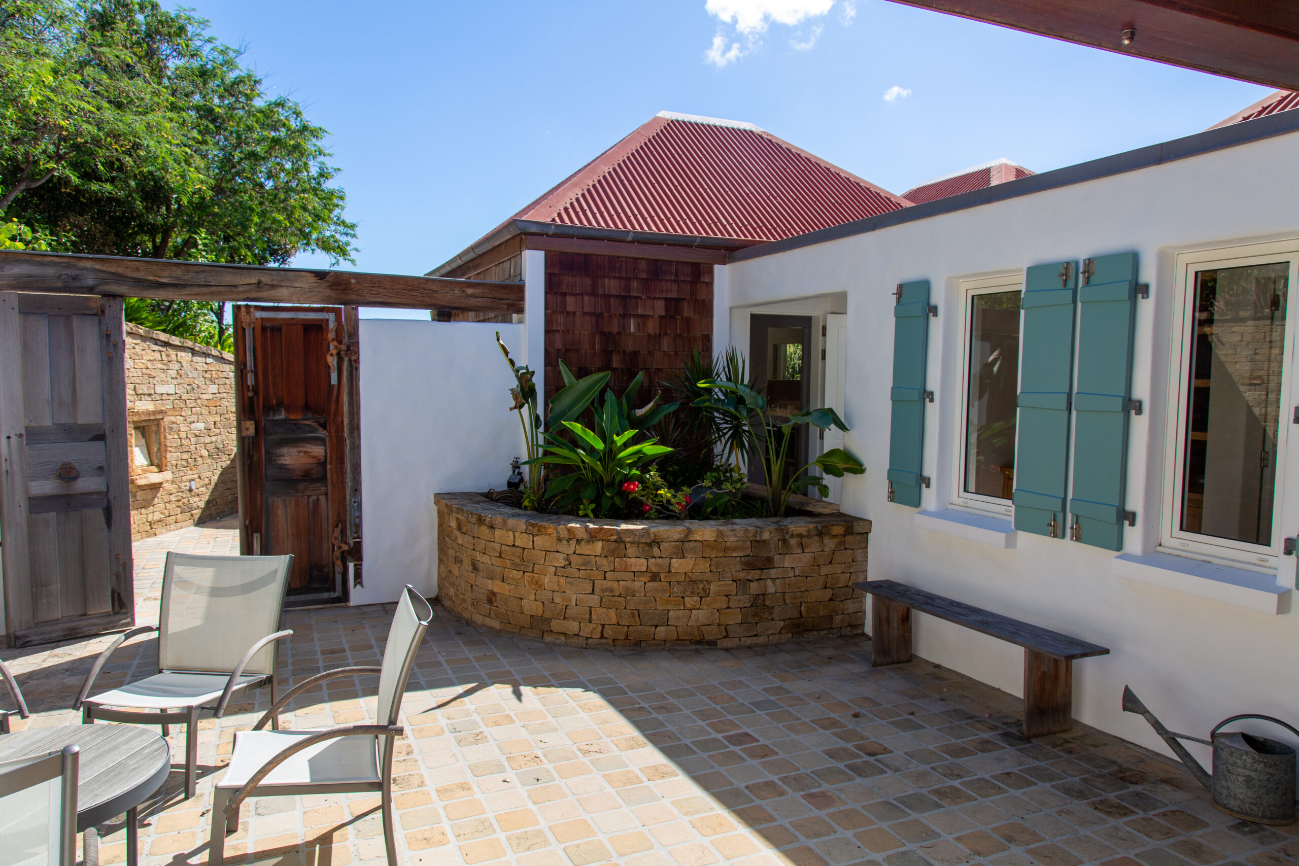 A secluded garden patio with chairs and a small brick planter filled with tropical plants.