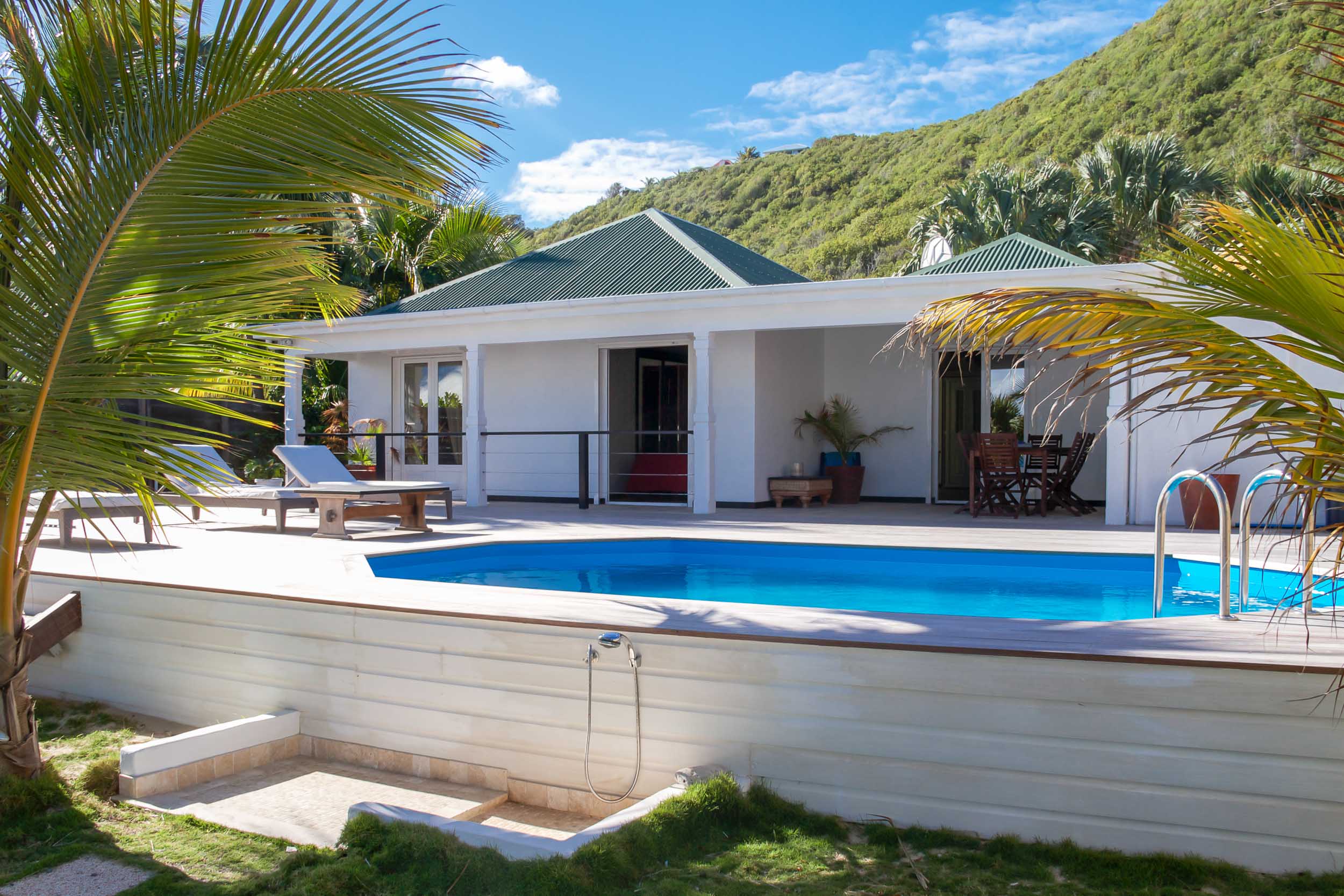 Charming St Barts villa with private pool, sun loungers, and hillside views framed by tropical palms.