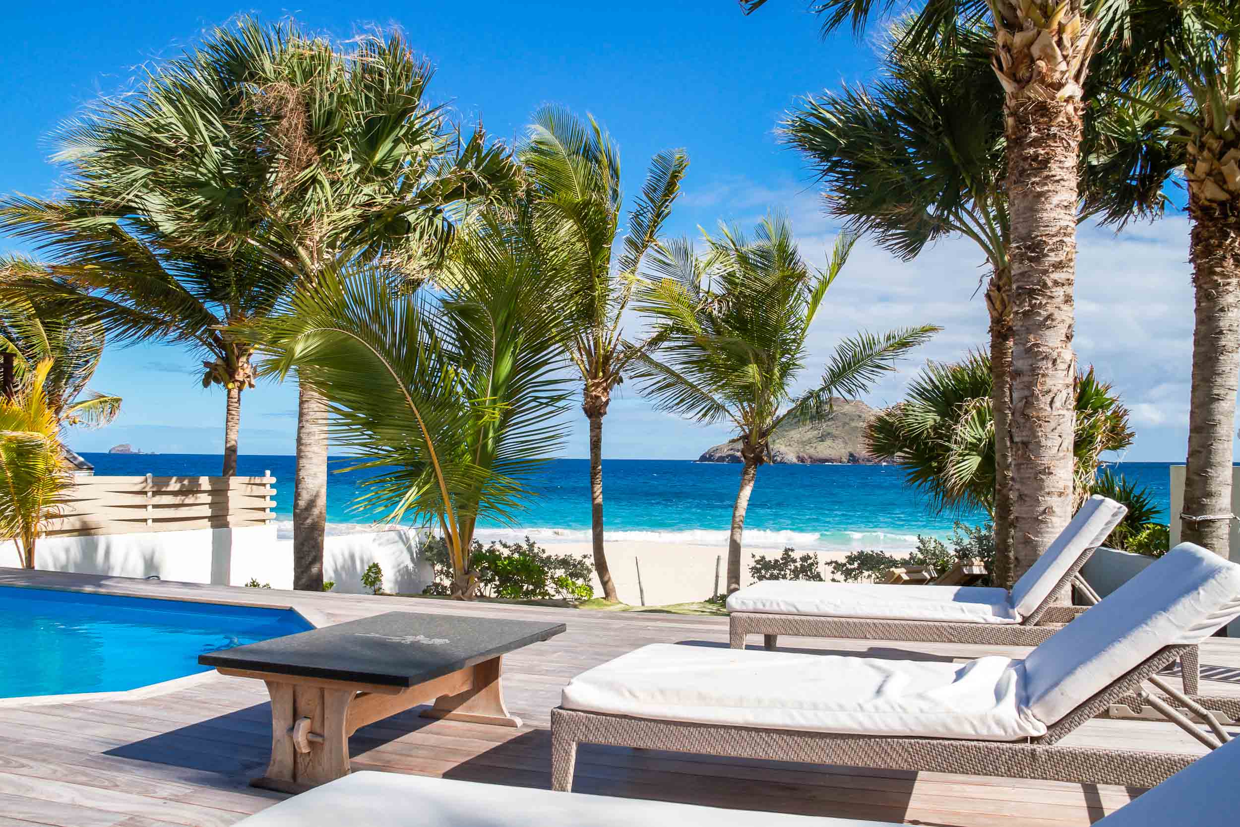 Beachfront St Barts villa with sun loungers by the pool, swaying palms, and turquoise Caribbean Sea views