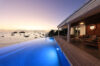 St Barts villa with illuminated infinity pool overlooking the bay at sunset, with terrace seating and ocean views.